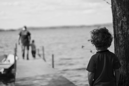 Photo of little boy standing away from the dock watching his dad and little brother walk the dock.  The intent shows fear.