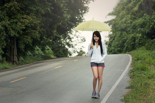 A young girl walking on a highway with an umbrella looking alone.  About age 16.